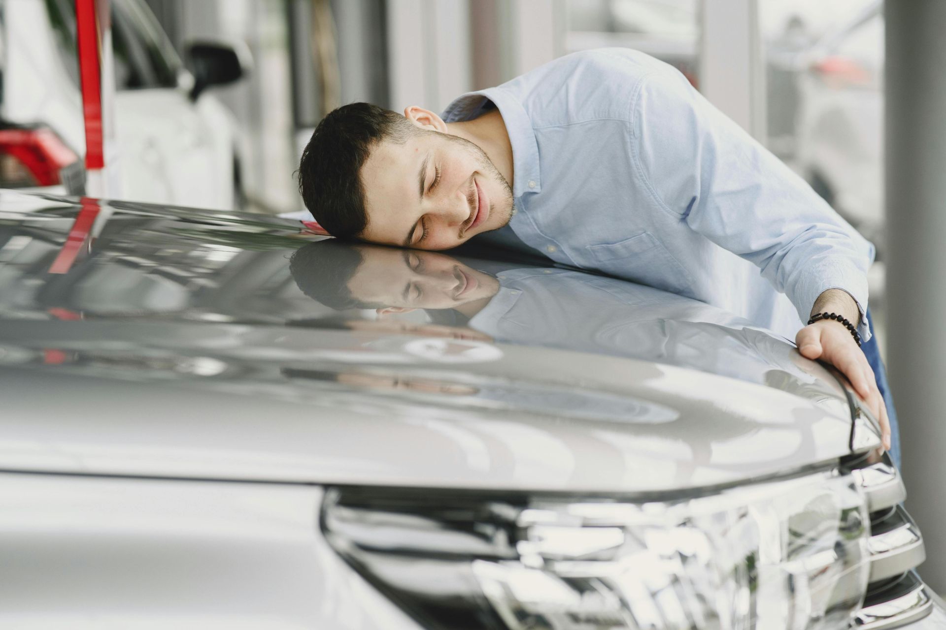A man joyfully embracing a new car indoors, reflecting happiness and satisfaction.