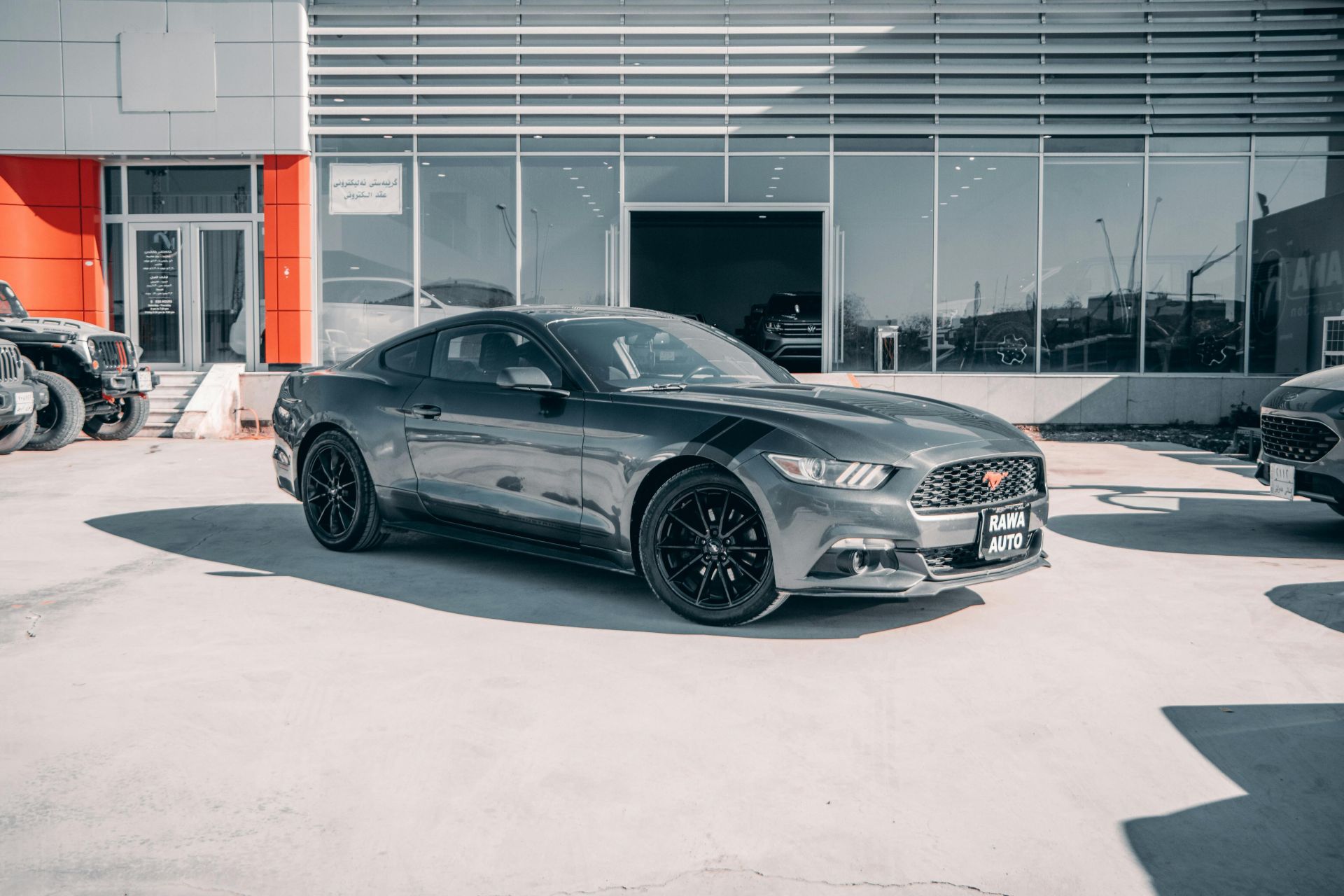 Sunlit view of a Ford Mustang parked outside an auto dealership with a modern facade.